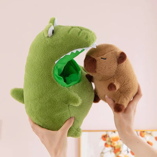 Green plush shark toy with a mouth opening, holding a small brown capybara plush animal against a light pink background.