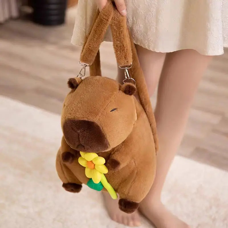 Brown plush bag shaped like a capybara with a flower, held by a person.