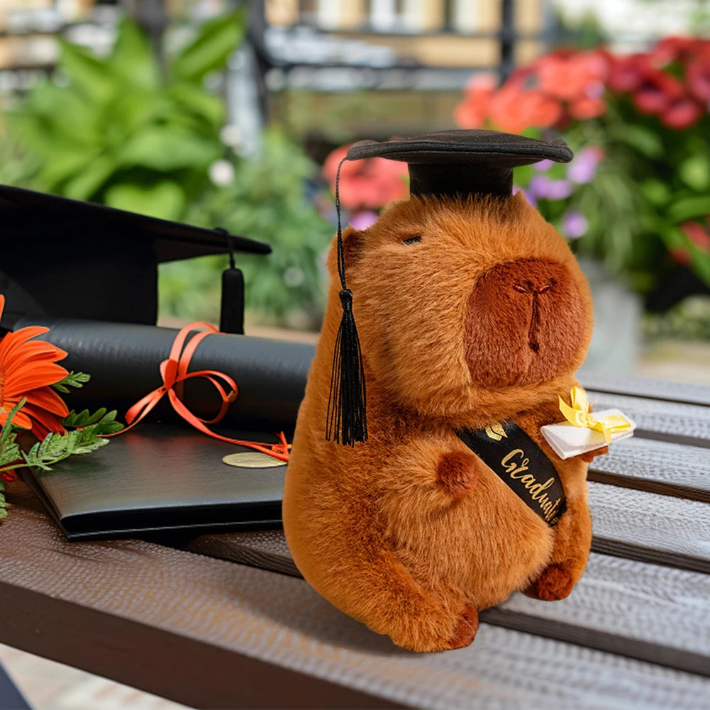 Plush capybara wearing a graduation cap and holding a diploma with a blurred outdoor background