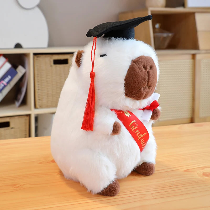 Plush toy capybara wearing a graduation cap and gown on a wooden surface