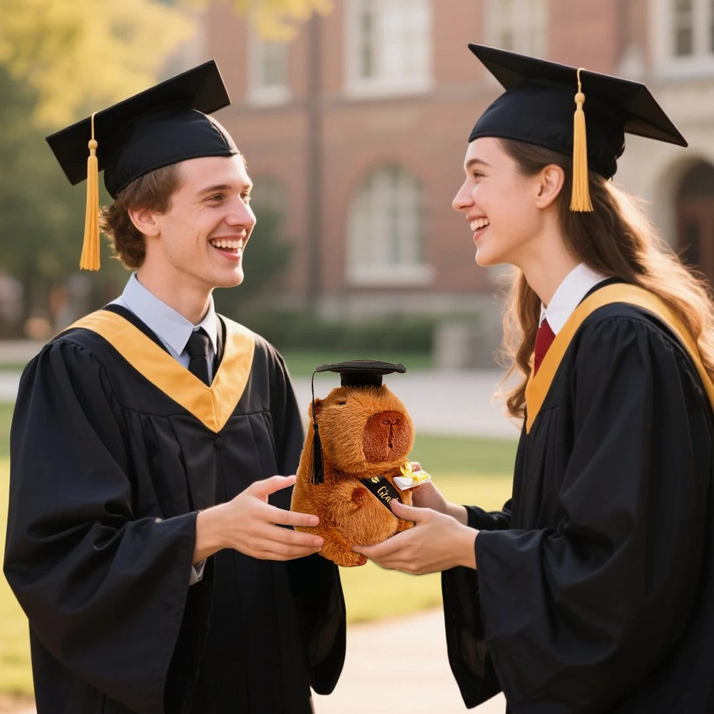Two graduates in caps and gowns holding a capybara with a graduation cap on it, outdoors.